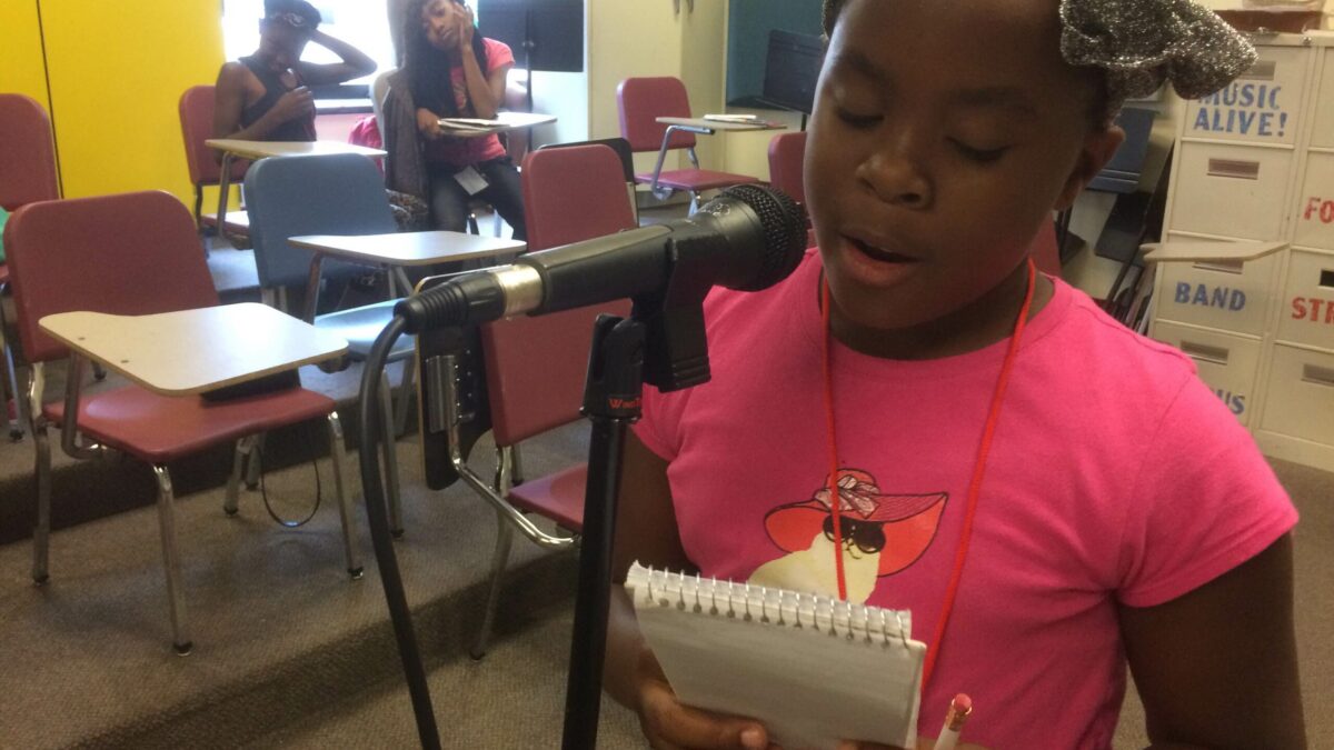 IMG_3126 A youth holding a notepad speaking into a microphone in a classroom