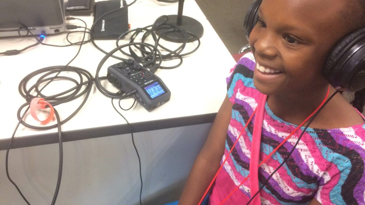 IMG_3145 A youth wearing headphones smiling sitting next to a portable recorder on a white table