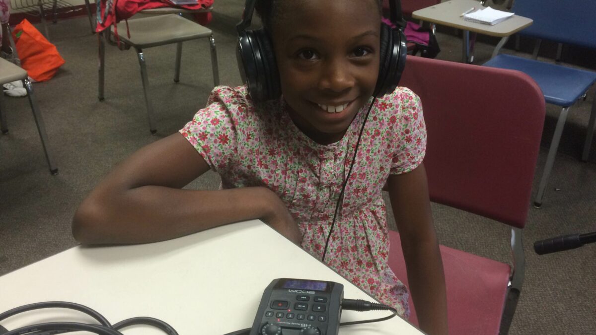 IMG_3147 A youth wearing headphones smiling sitting behind a portable recorder in a classroom
