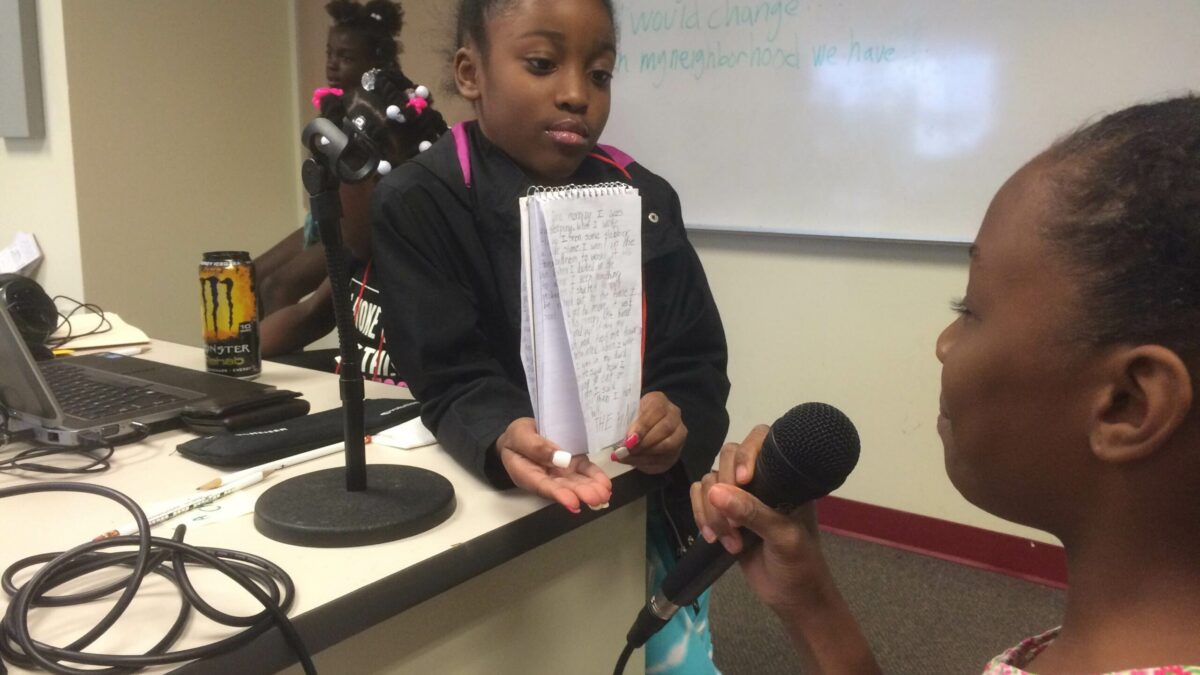 IMG_3151 A youth holding a notebook open for a youth holding a microphone in a classroom