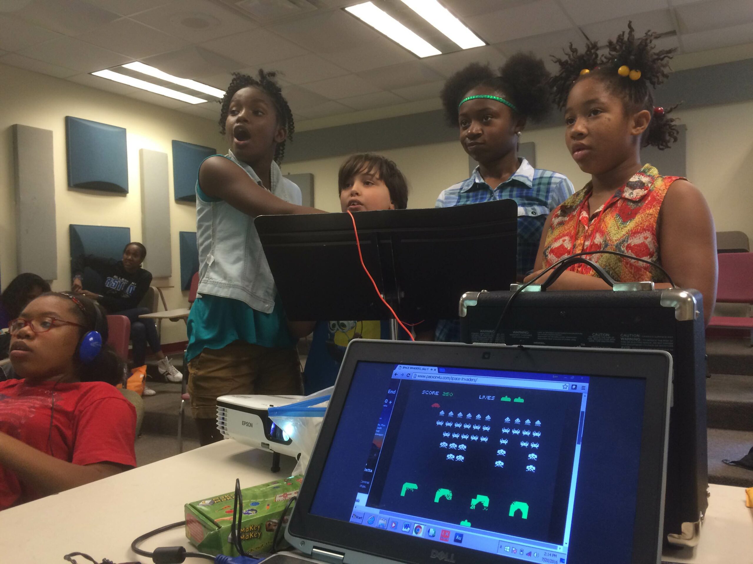 Four youth standing behind a music stand, one speaking into a microphone