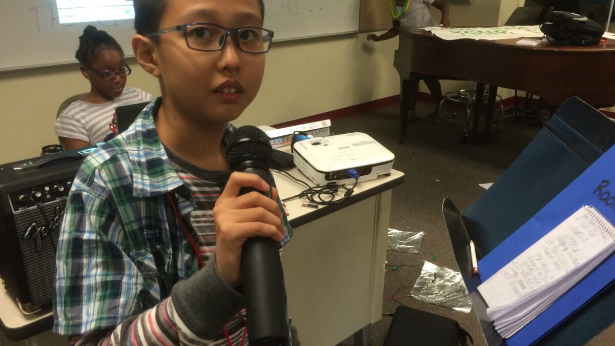 A youth holding a microphone standing next to a music stand