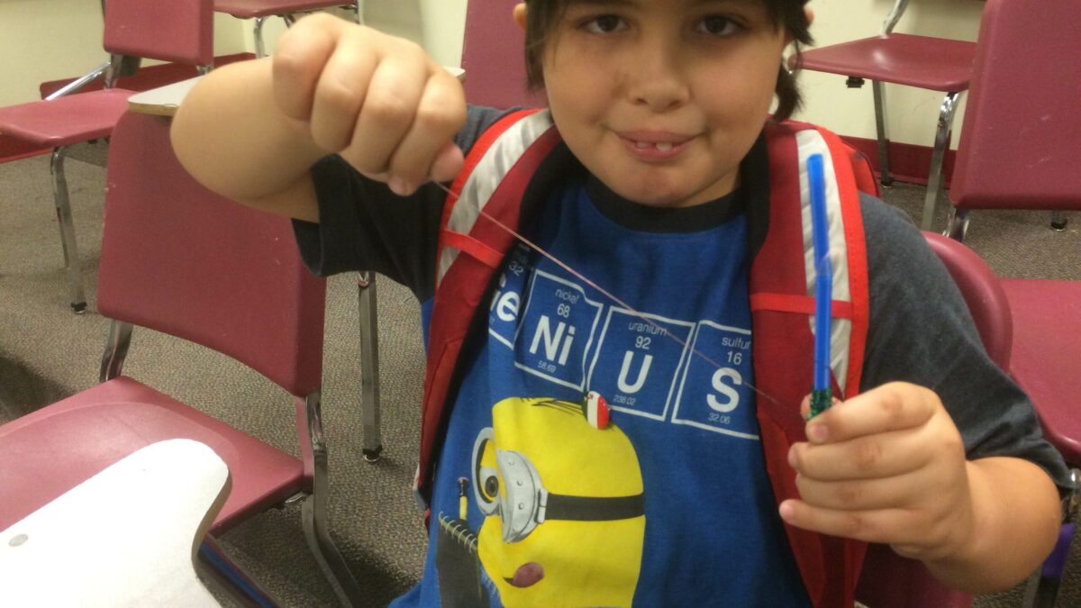 A youth holding a piece of string tied to a small blue cylinder