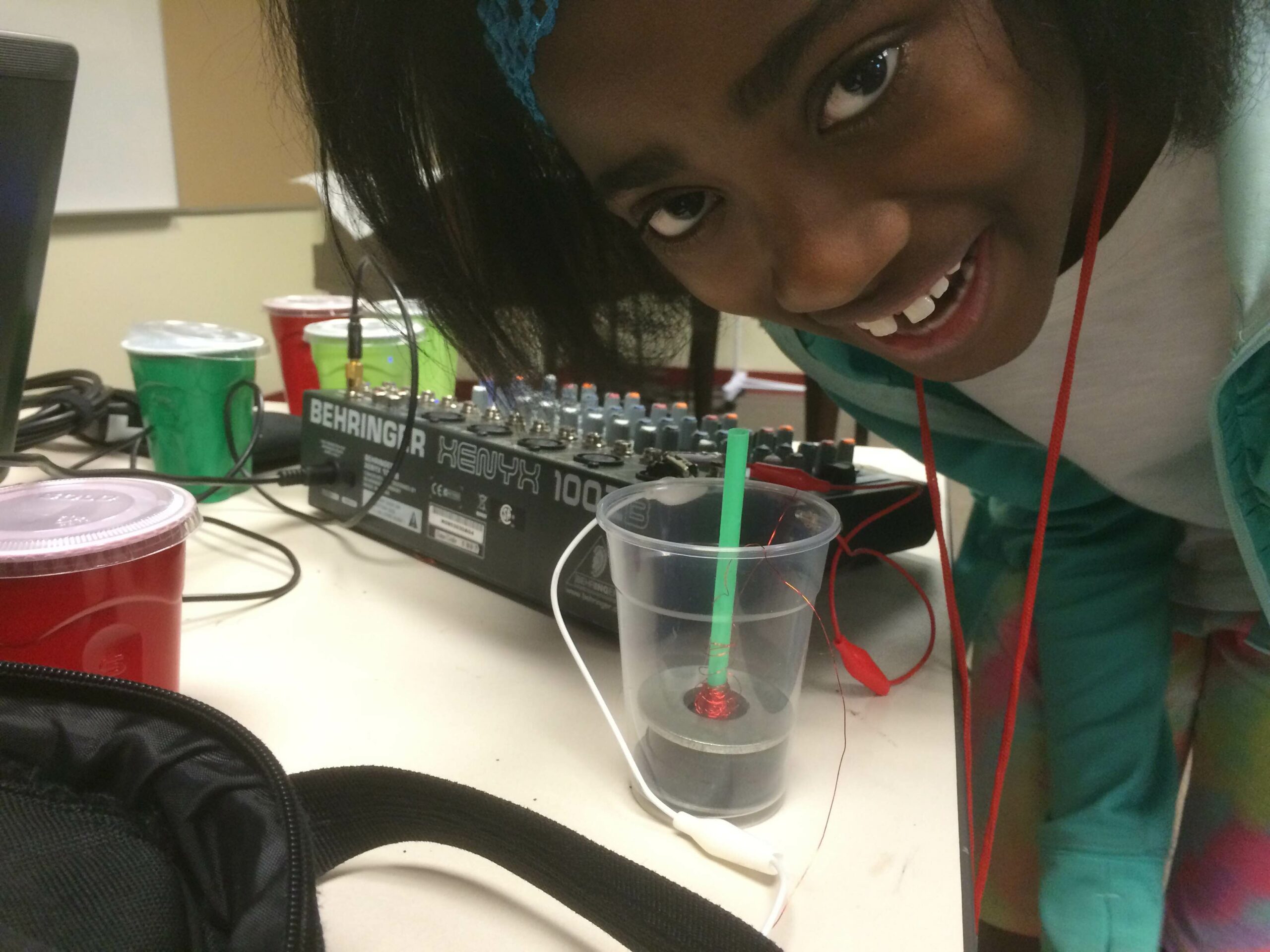 A youth crouched over a mixer speaking into a plastic cup with a thin cylinder inside