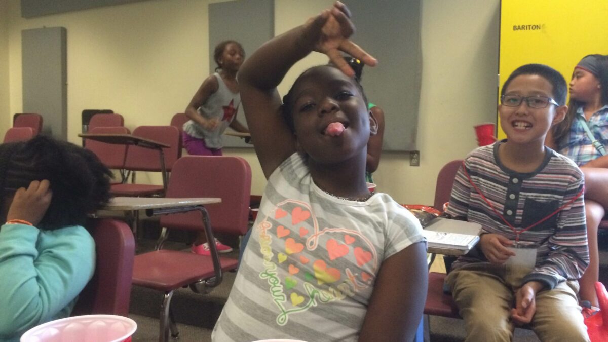 A youth flashing a piece sign and sticking out their tongue and four youth sitting in the background