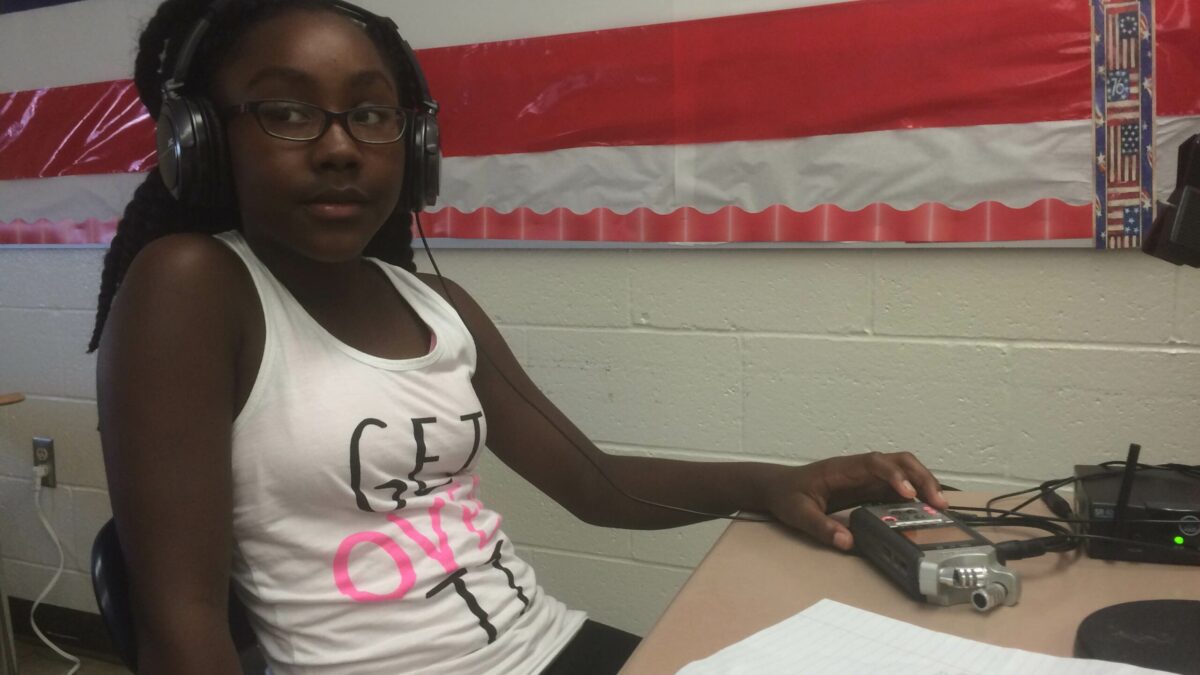 A youth wearing headphones interacting with a portable recorder sitting on a classroom desk