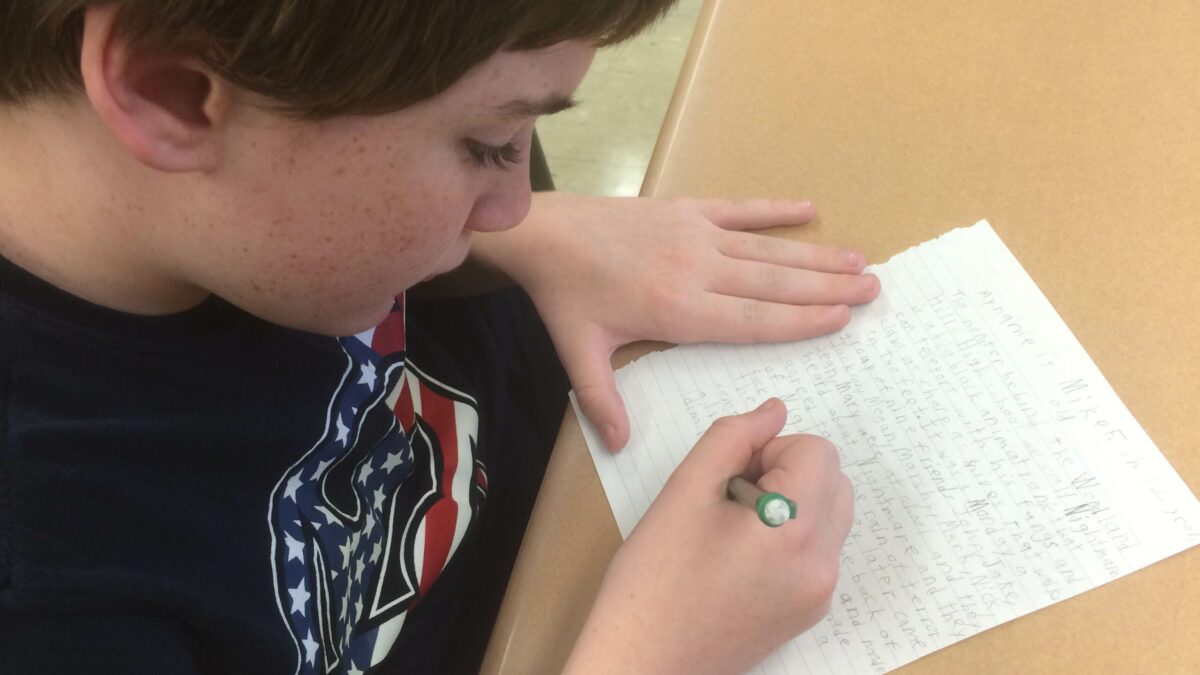 A youth writing on a piece of notebook paper on a classroom desk