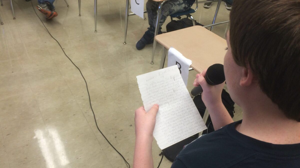 A youth reading a piece of paper and holding a microphone in a classroom