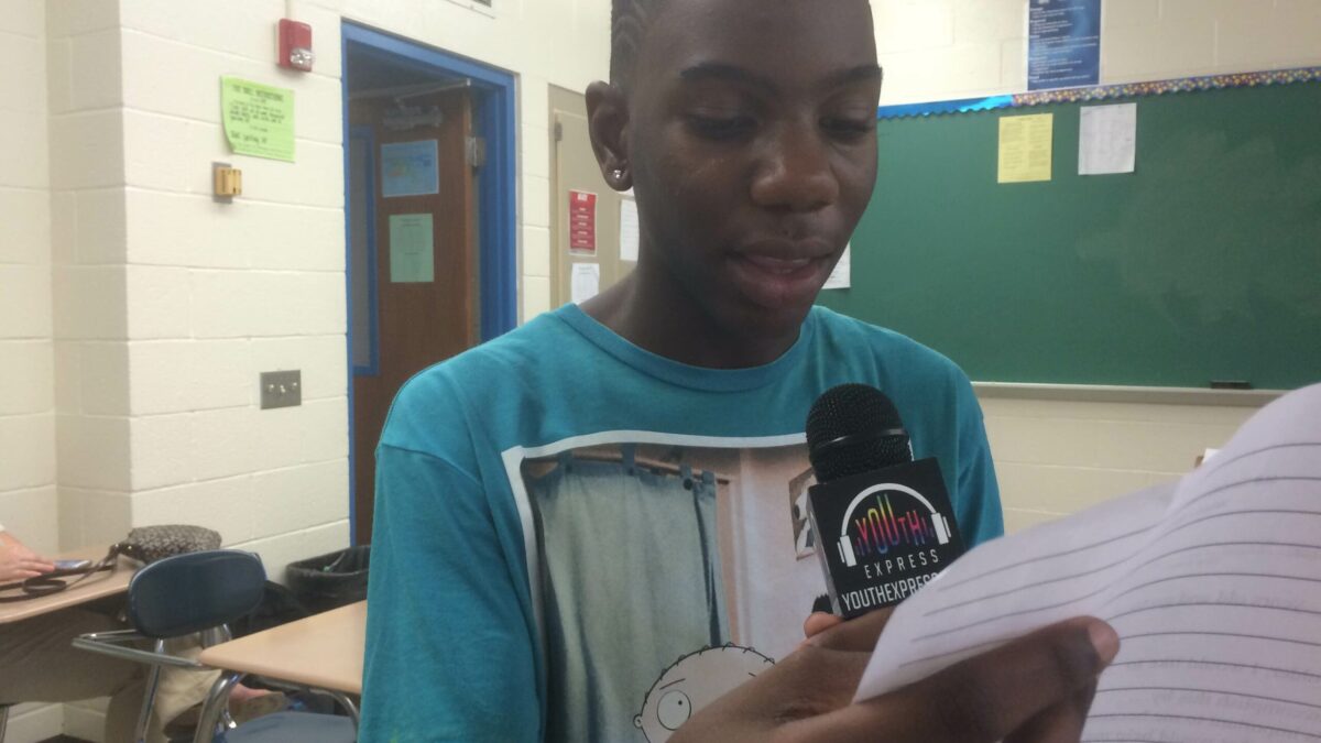 A youth holding a piece of paper and speaking into a microphone in a classroom