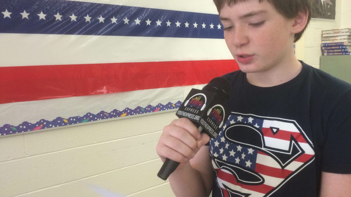 A youth holding a piece of paper and speaking into a microphone in a classroom