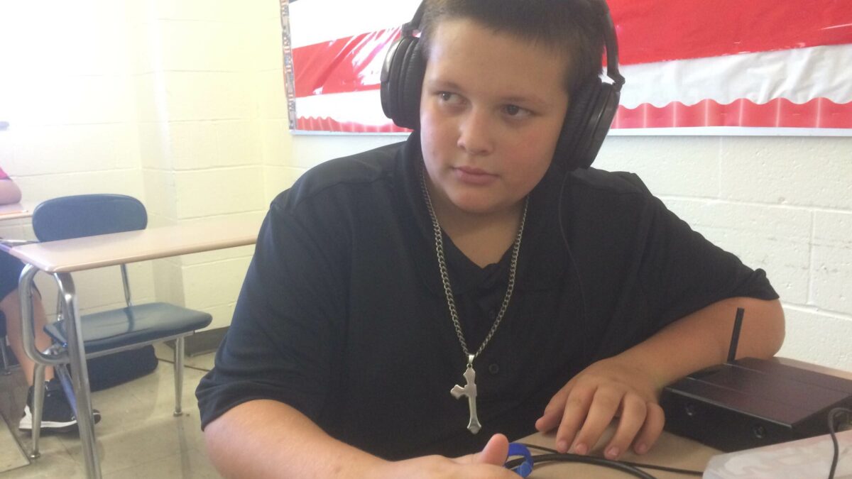 A youth wearing headphones interacting with a portable recorder sitting at a classroom desk