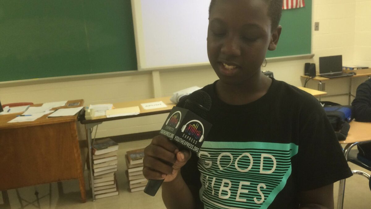 A youth holding a piece of paper and speaking into a microphone in a classroom