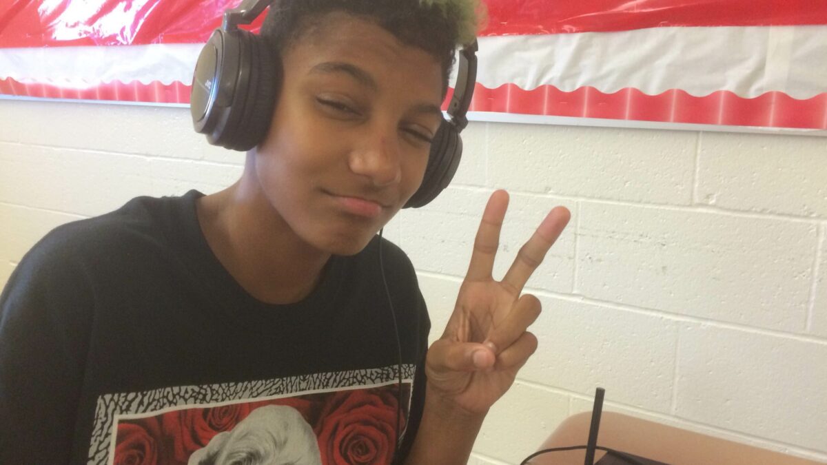 A youth wearing headphones flashing a peace sign with their fingers in a classroom