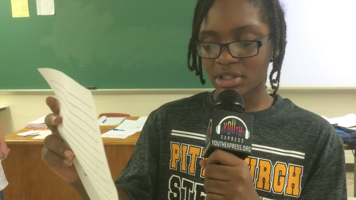 A youth holding a piece of paper and speaking into a microphone in a classroom