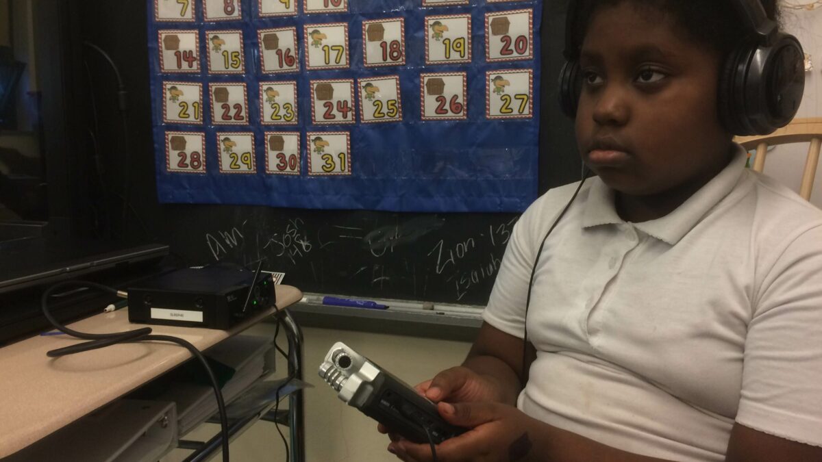 A youth wearing headphones holding a portable recorder in a classroom