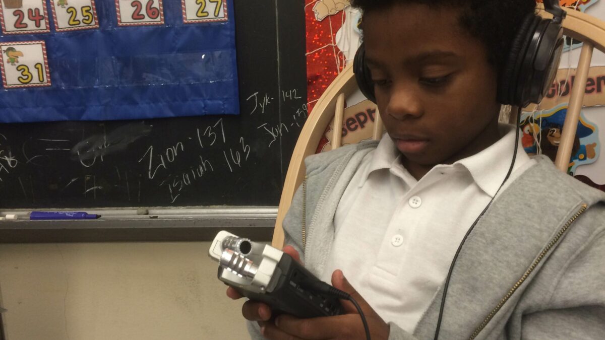 A youth wearing headphones holding a portable recorder in a classroom