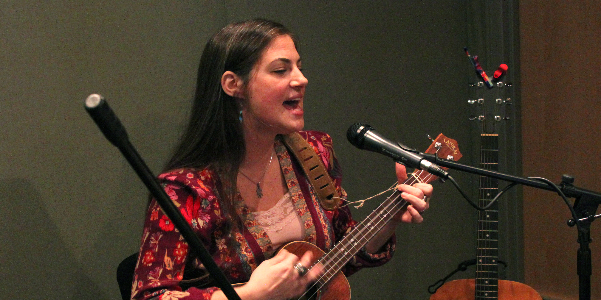 An adult playing acoustic guitar and singing into a microphone in a radio studio