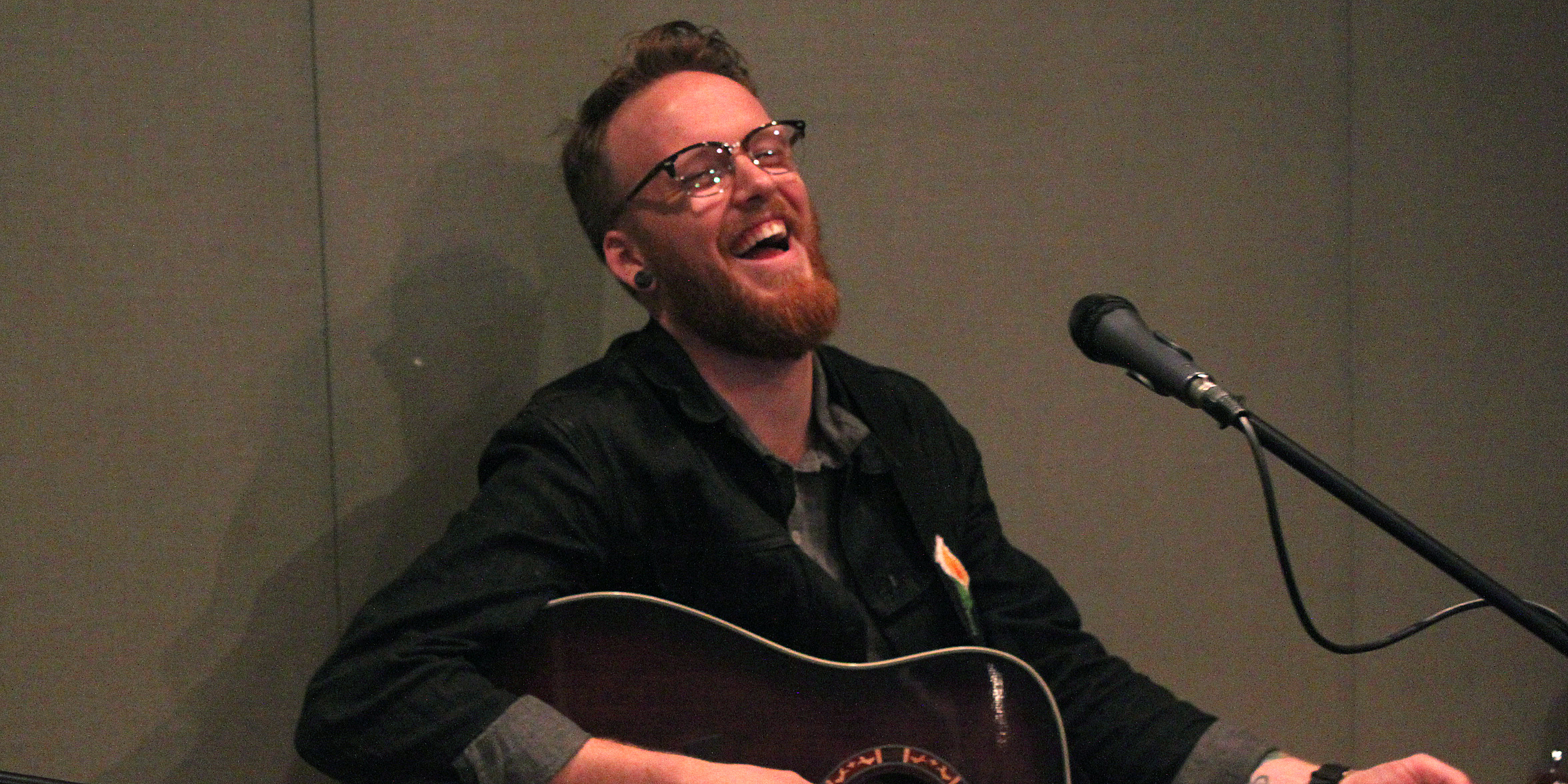 An adult playing acoustic guitar and singing into a microphone in a radio studio