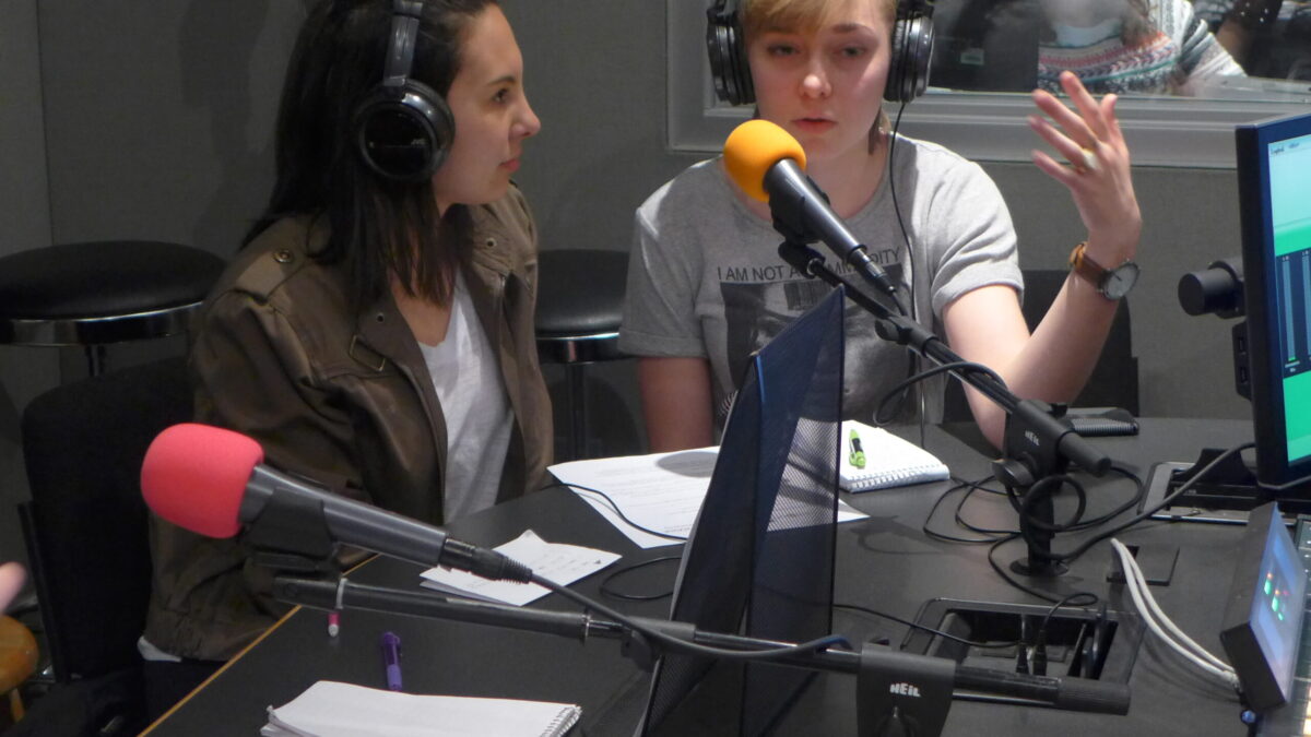 Two teens wearing headphones speaking into microphones in a radio studio