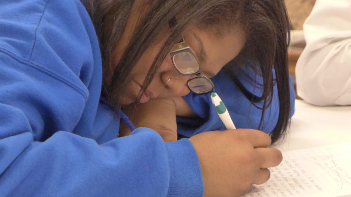 A teen writing onto a piece of paper on a white table