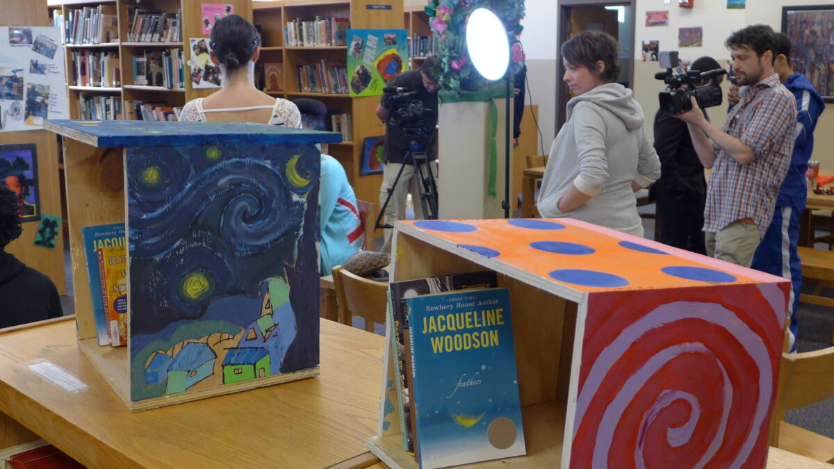 A blue box covered in painted stars and a red box with a white painted spiral, both containing books in a library