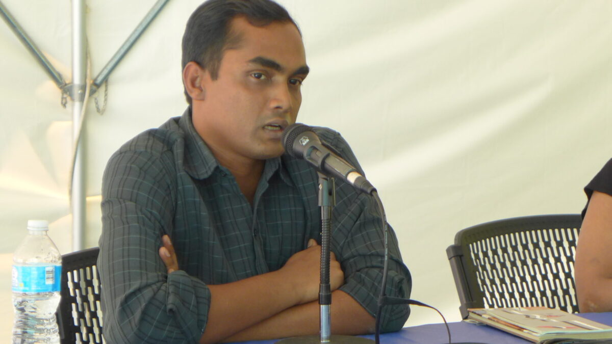 An adult sitting and speaking into a microphone