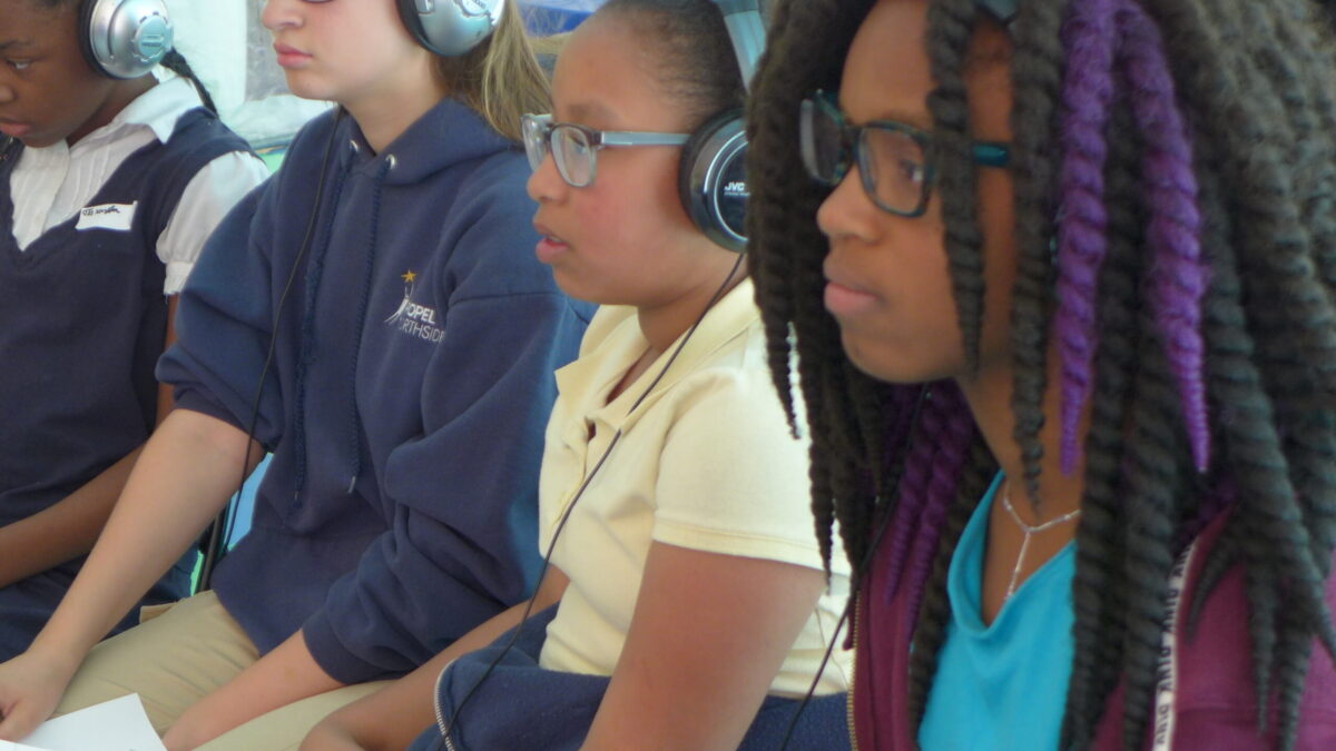 Four youth sitting holding pieces of paper, three of the youth wearing headphones