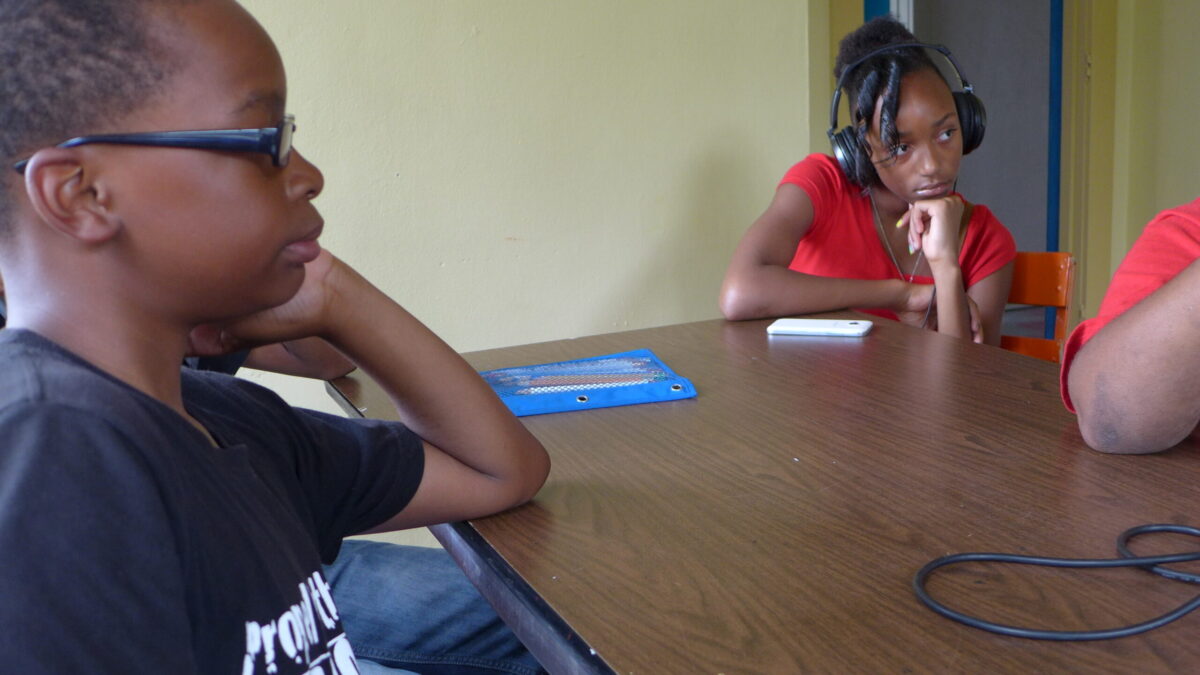 Two youth sitting around a brown table, one youth wearing headphones