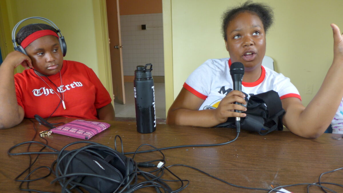 A youth wearing headphones listening to a youth holding and speaking into a microphone