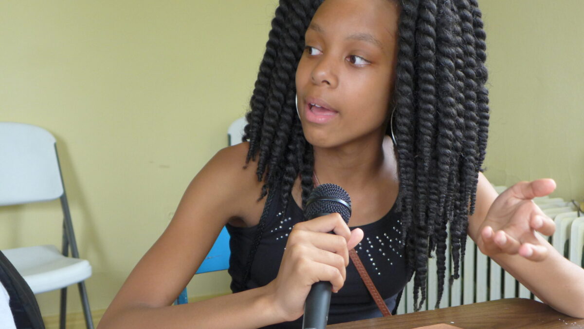 A youth holding and speaking into a microphone and gesturing with their hand