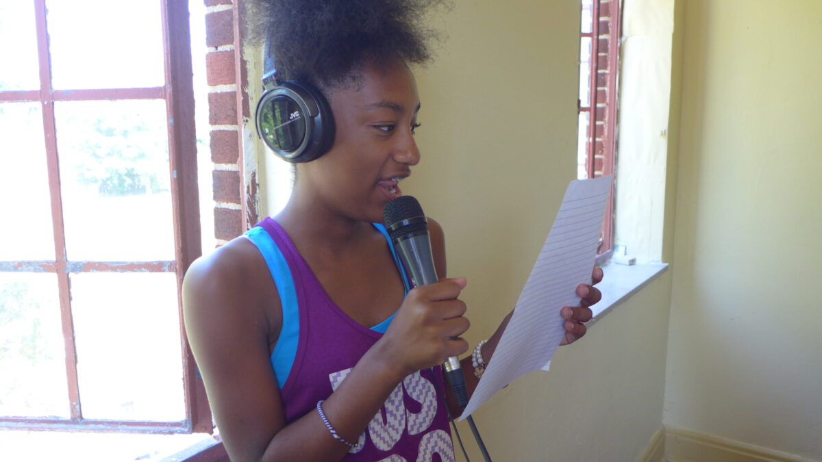 A youth wearing headphones holding a microphone and reading a piece of paper