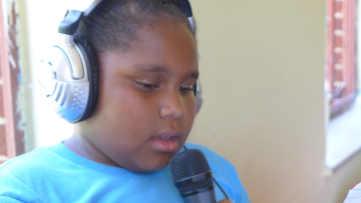 A youth wearing headphones holding and speaking into a microphone