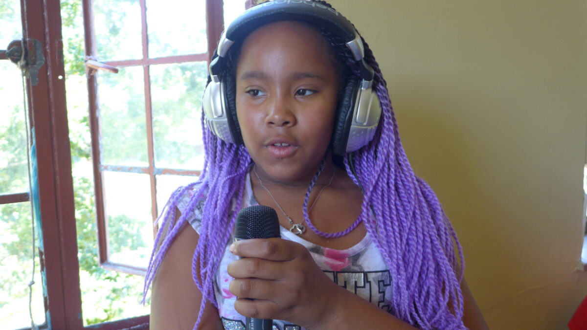 A youth wearing headphones holding and speaking into a microphone