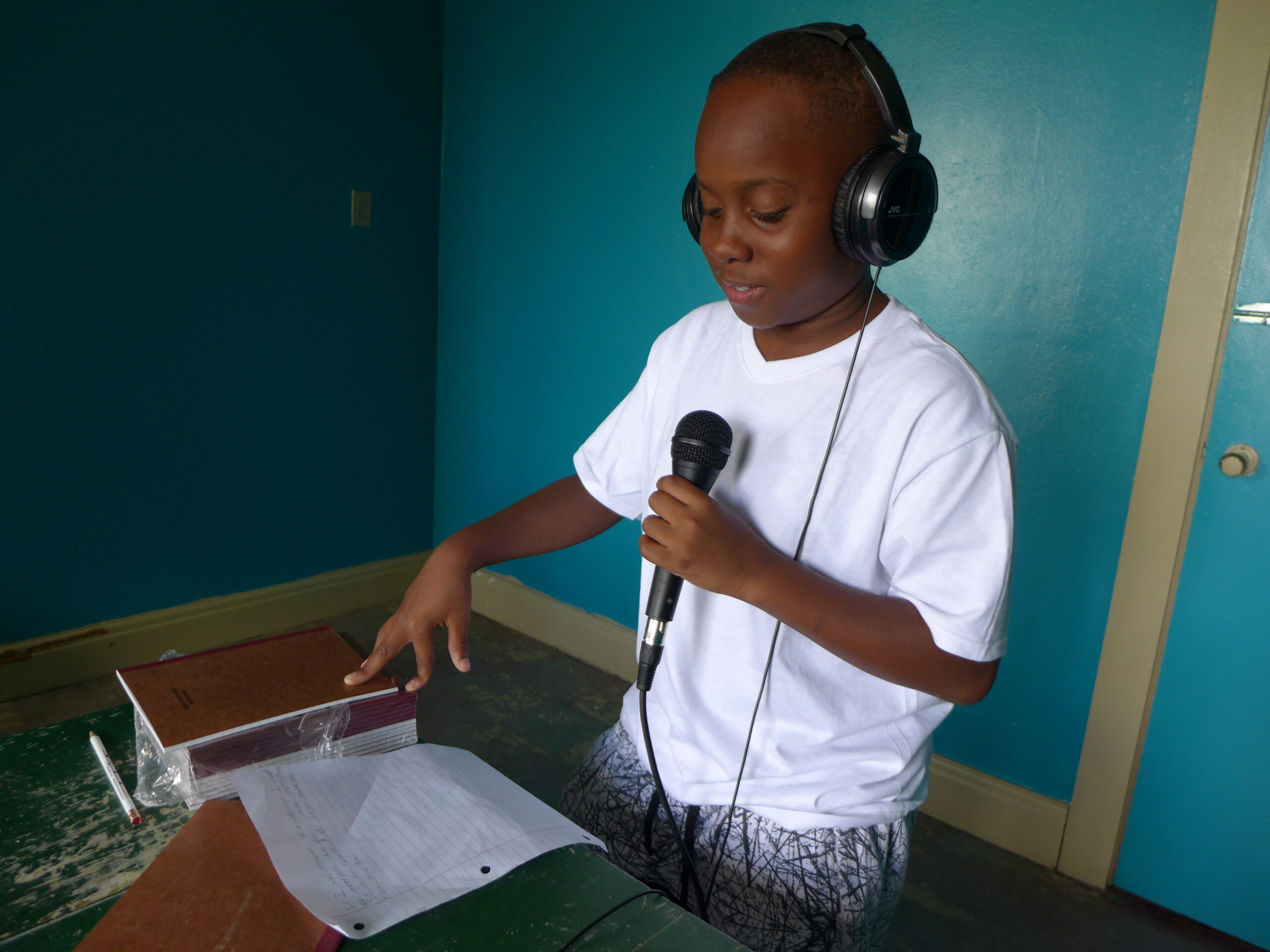 A youth wearing headphones holding a microphone looking down at a piece of paper