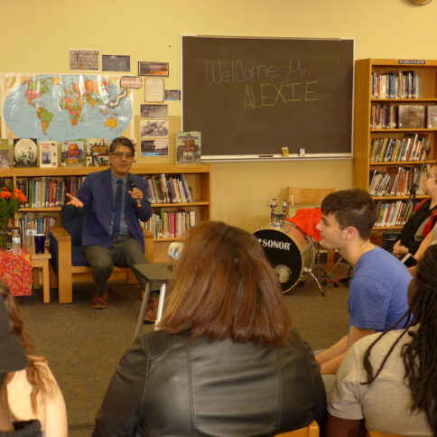 An adult and a youth listening to another youth present in front of a classroom