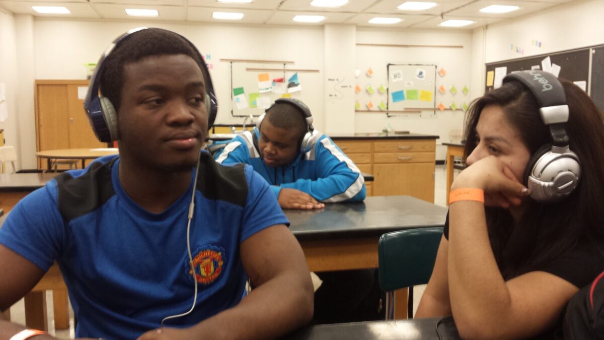 Three teens wearing headphones sitting at classroom desks