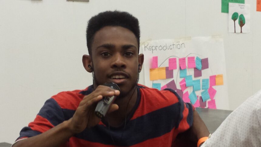 A teen holding and speaking into a portable recorder in a classroom