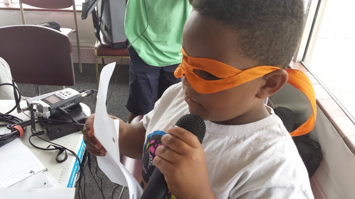 20150706_103229 A youth wearing an orange eye mask reading a piece of paper and holding a microphone
