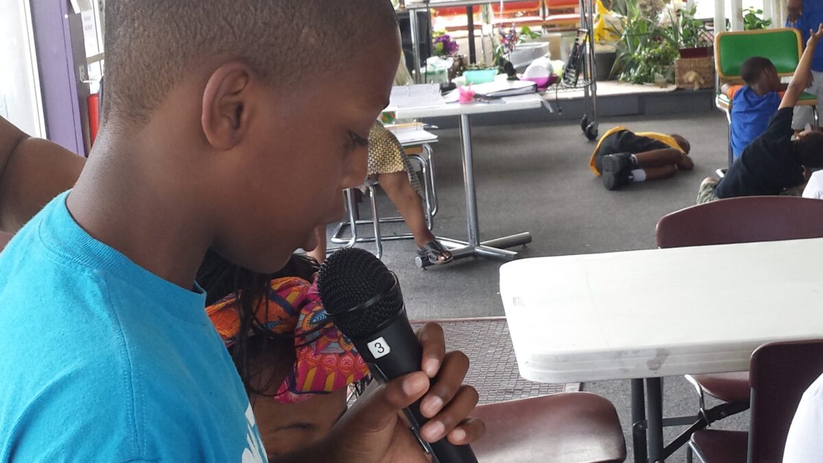 A youth looking down holding and speaking into a microphone