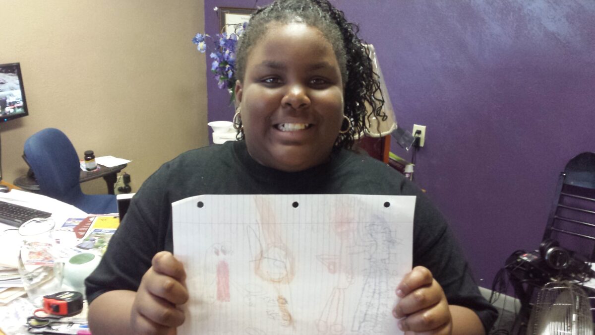 A youth holding a piece of paper smiling at the camera in front of a purple wall