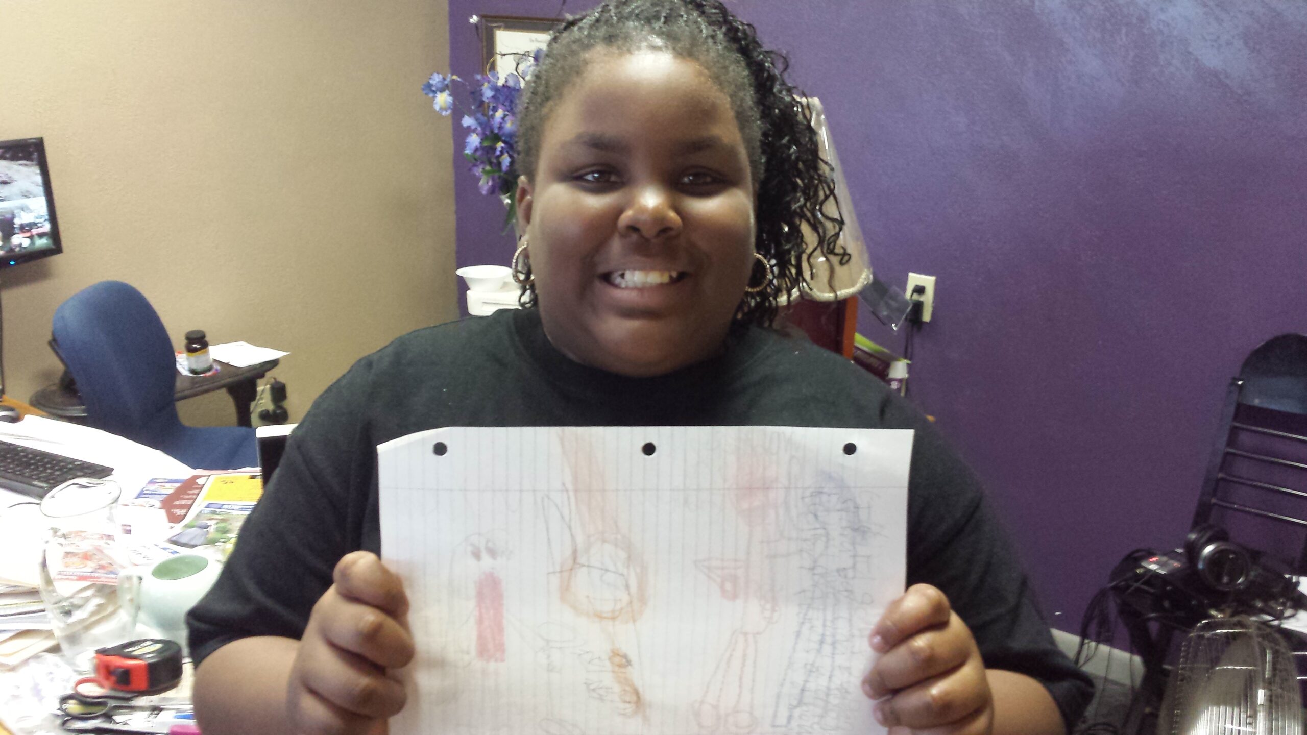 A youth holding a piece of paper smiling at the camera in front of a purple wall