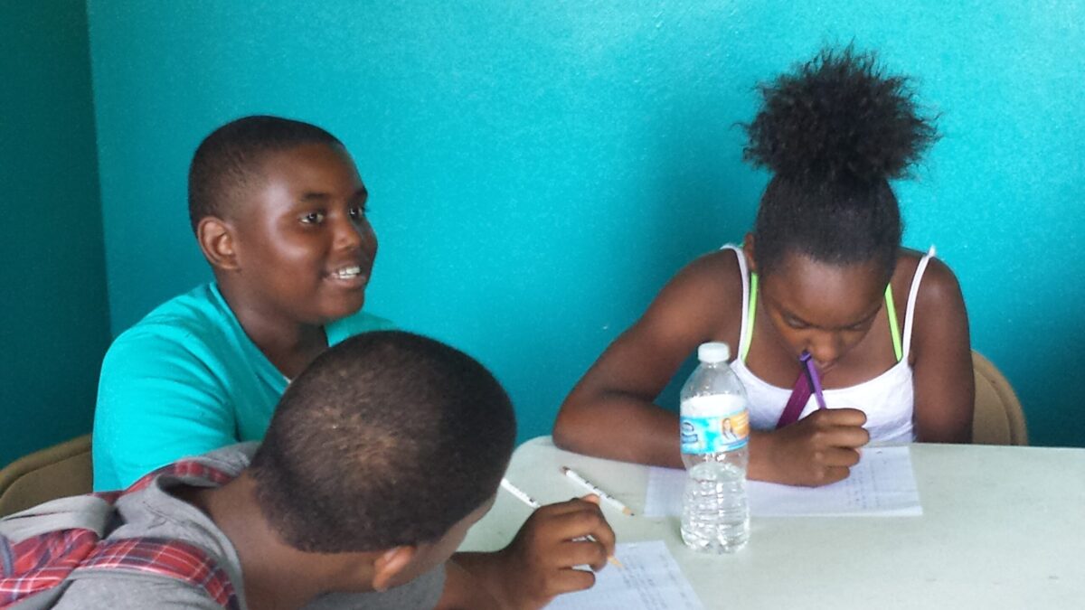 Three youths writing on pieces of paper on a white table in a blue room