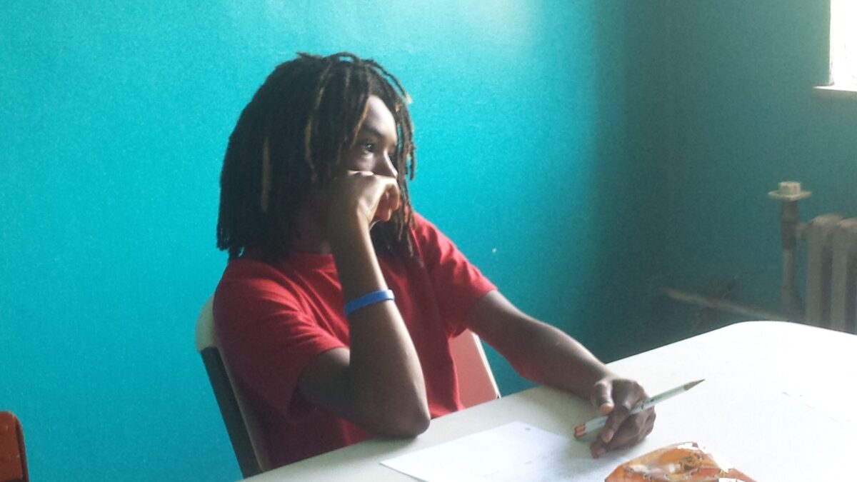 A youth holding a pencil sitting at a white table in a blue room