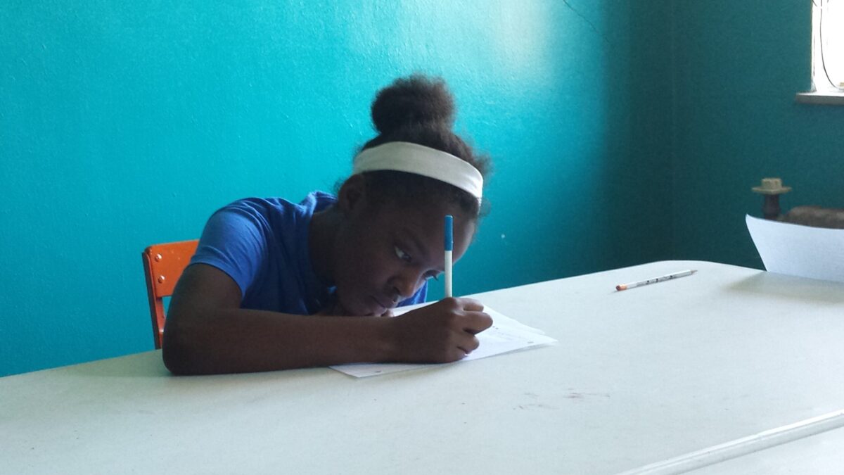A youth writing on a piece of paper on a white table in a blue room