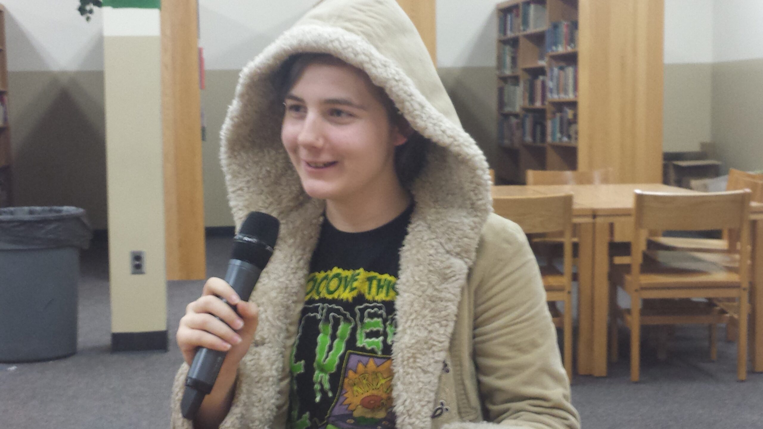 A teen holding and speaking into a microphone in a library