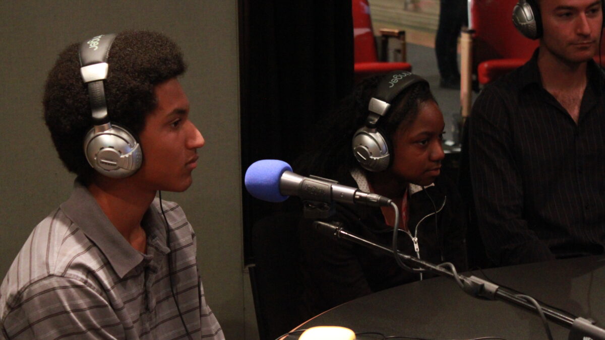 IMG_0102 Two teens and an adult wearing headphones sitting behind microphones in a radio studio