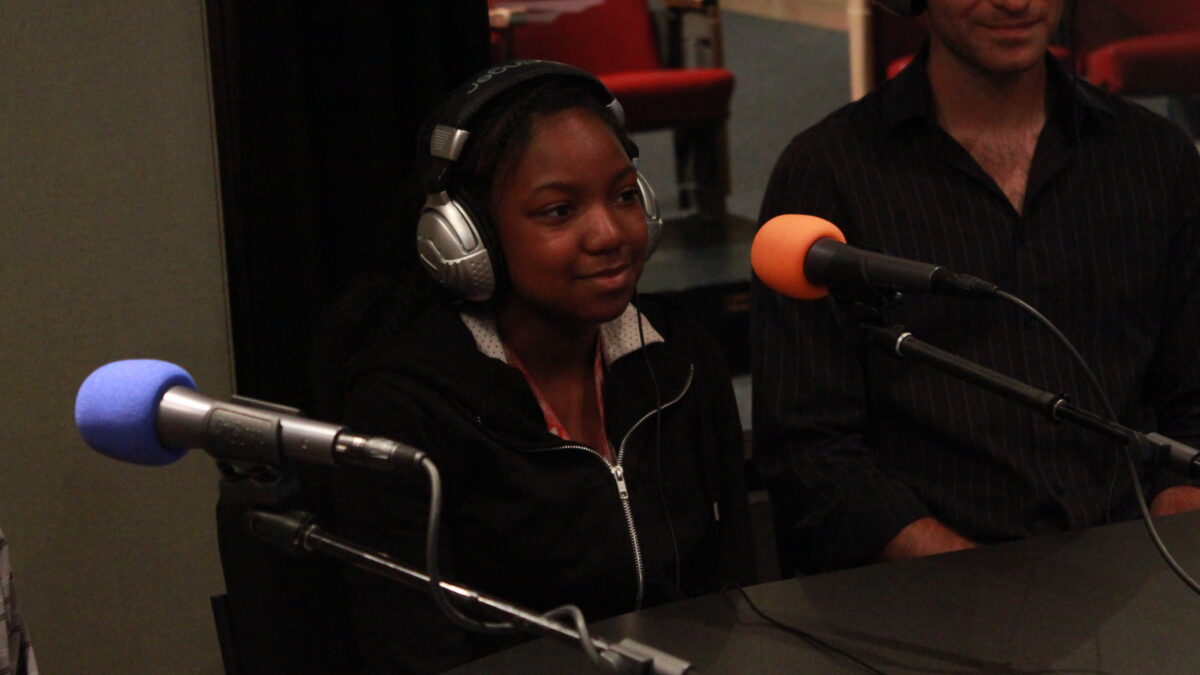 IMG_0104 A teen and an adult wearing headphones sitting behind microphones in a radio studio