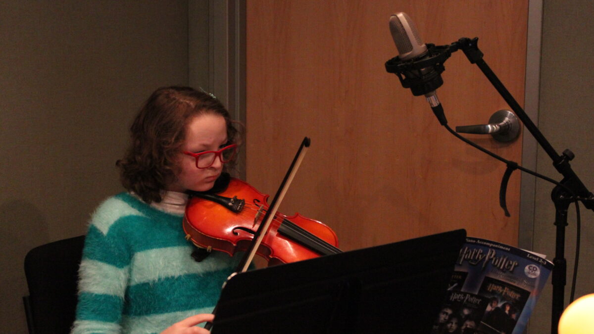 IMG_0441 A youth playing a violin looking at sheet music on a music stand in a radio studio