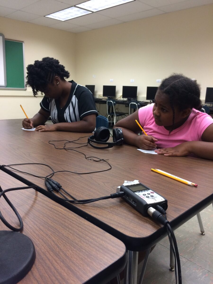 IMG_0547 Two youth writing on pieces of paper on a brown table in a classroom