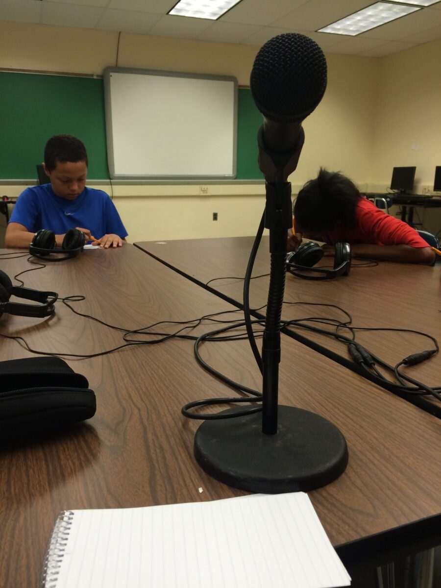 IMG_0548 A closeup of a microphone and two youth writing on pieces of paper on a brown table in the background